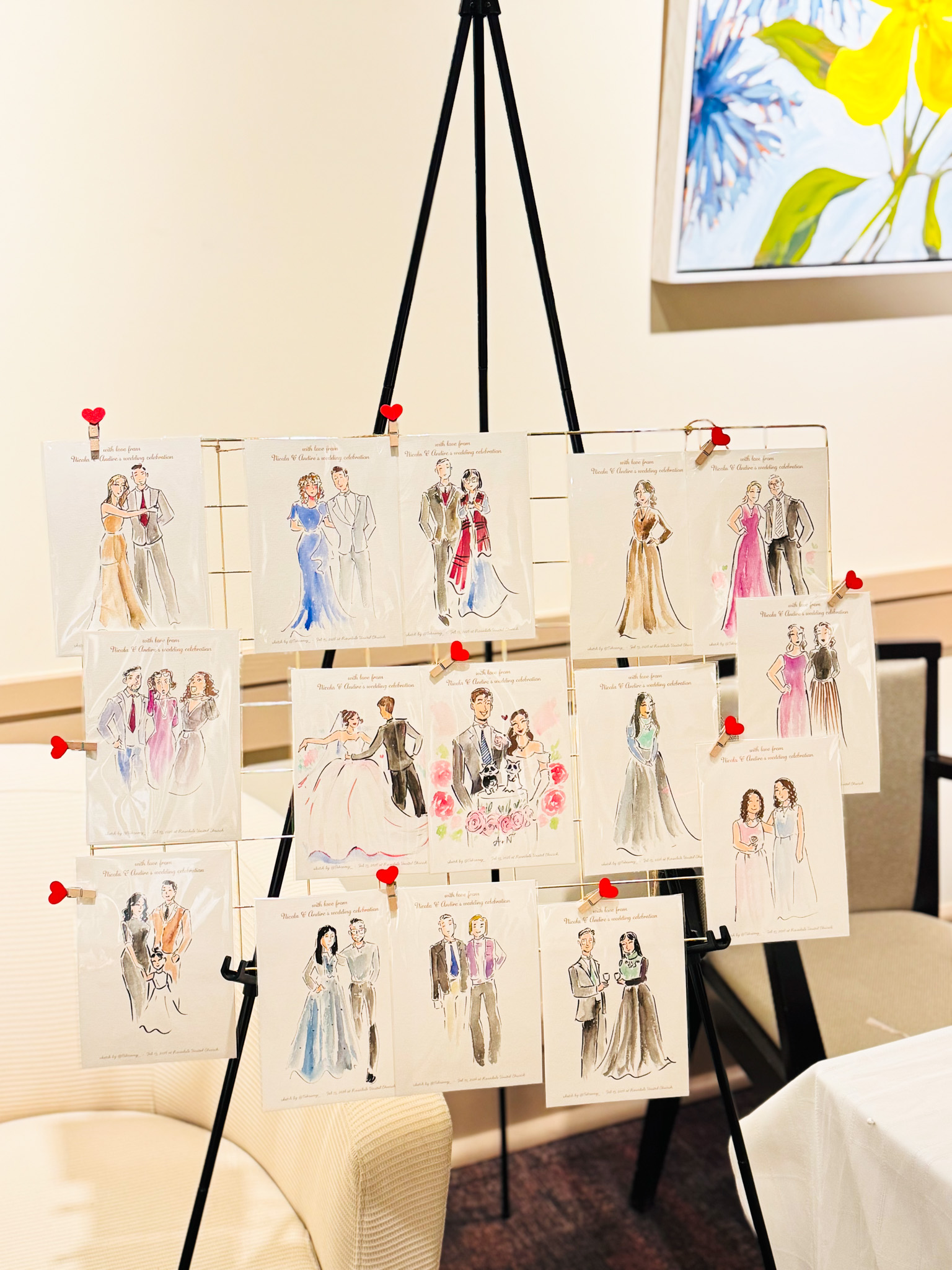Live wedding guest sketches displayed on an easel by Toronto live illustrator Tehremy, featuring hand-drawn fashion portraits clipped with red heart pins at a wedding reception.