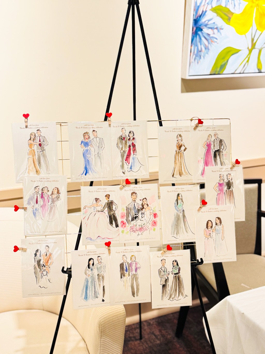 Live wedding guest sketches displayed on an easel by Toronto live illustrator Tehremy, featuring hand-drawn fashion portraits clipped with red heart pins at a wedding reception.